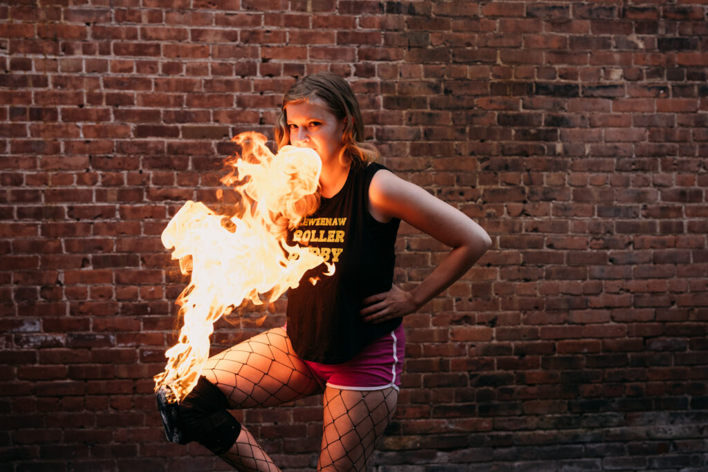 Scrambled Legs posing in front of a brick wall with fire coming from her knee.